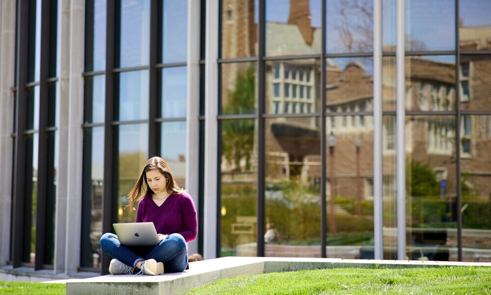 student sitting outside and working on laptop